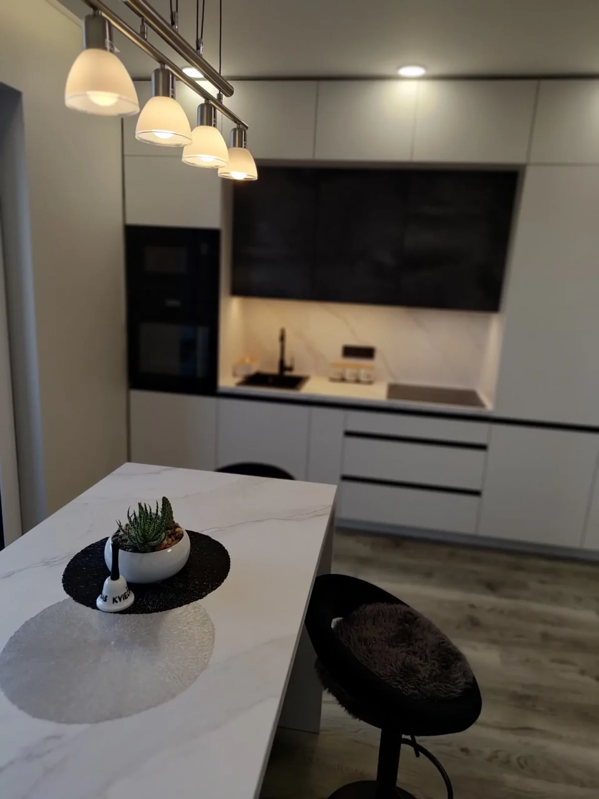 Pilna Vidaus Apdaila Kaune Kreves Prospekte Vakarinė Virtuvė Su šviestuvų šviesa Ir Marmuro Baro Sala Priešais Pilką Spintelių Kombinaciją